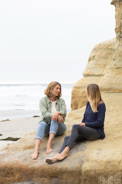 Two women sitting together on the beach — warmth and support